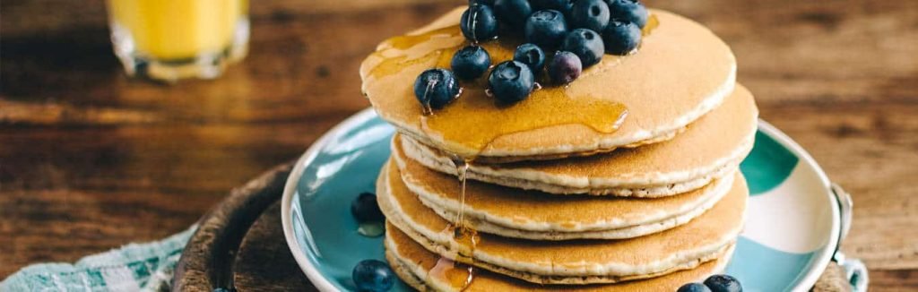 Uova a colazione sotto forma di pancake con sciroppo e mirtilli